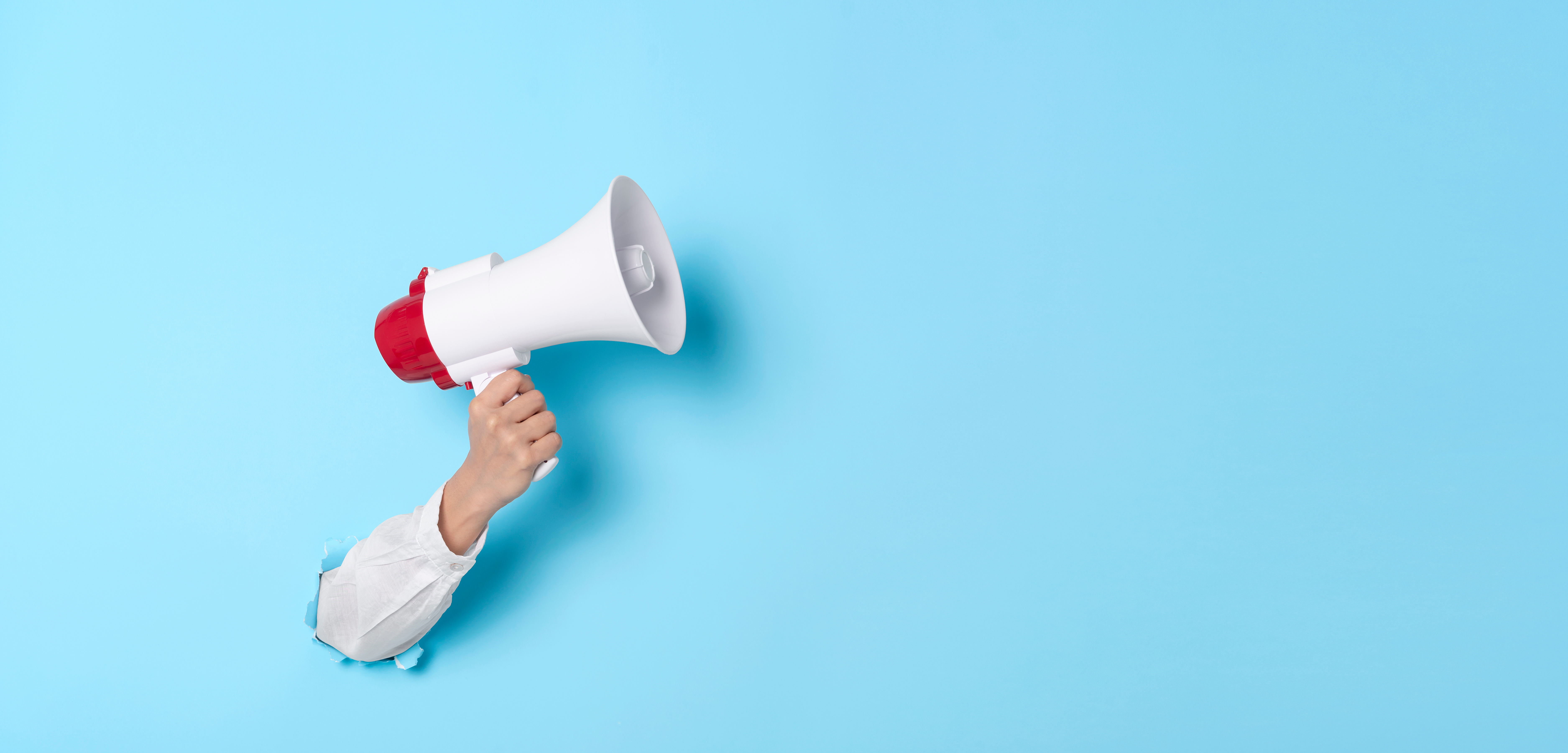 Business Hand holds a megaphone from a hole in the wall on blue background.  hiring, advertising, advertise and Banner concept.